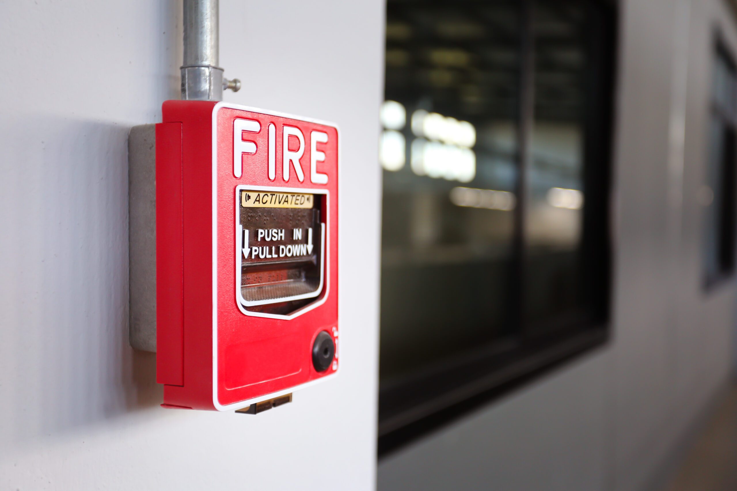 Red fire alarm box mounted on a white wall near a window, with instructions to "push in pull down" visible on the front.